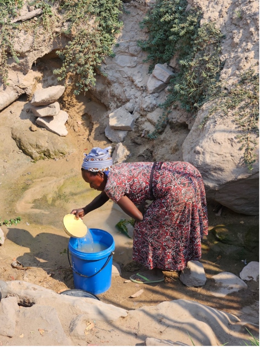 A woman bending to fill a bucket of water from a borehole in the Saba/Lubanda Ward in Binga District.